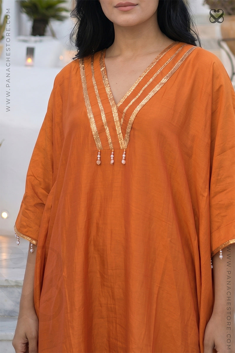 Woman wearing an orange kaftan dress with gold embroidery outdoors.