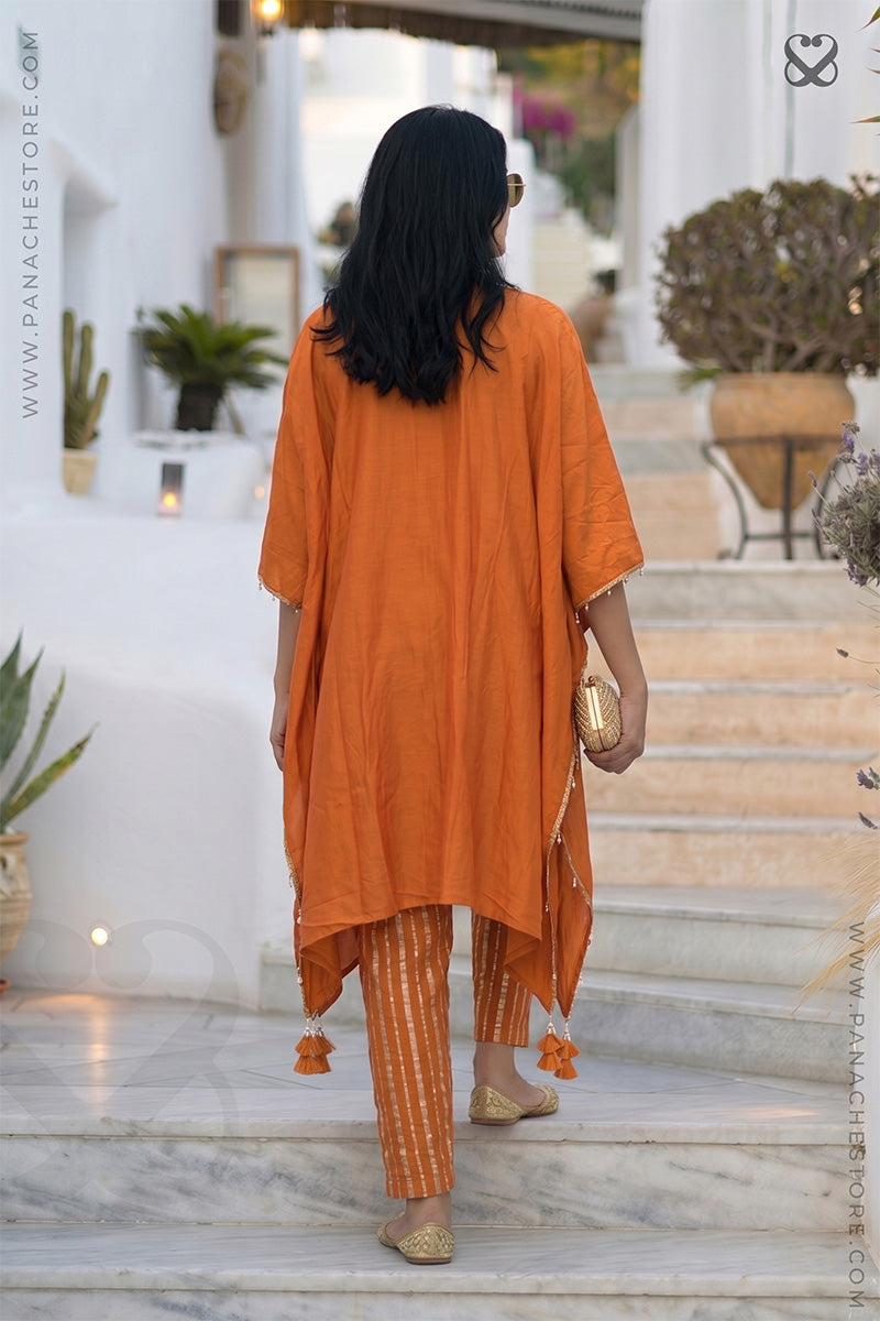 Woman in an orange Kaftan and zari strip orange pant outfit walking on steps