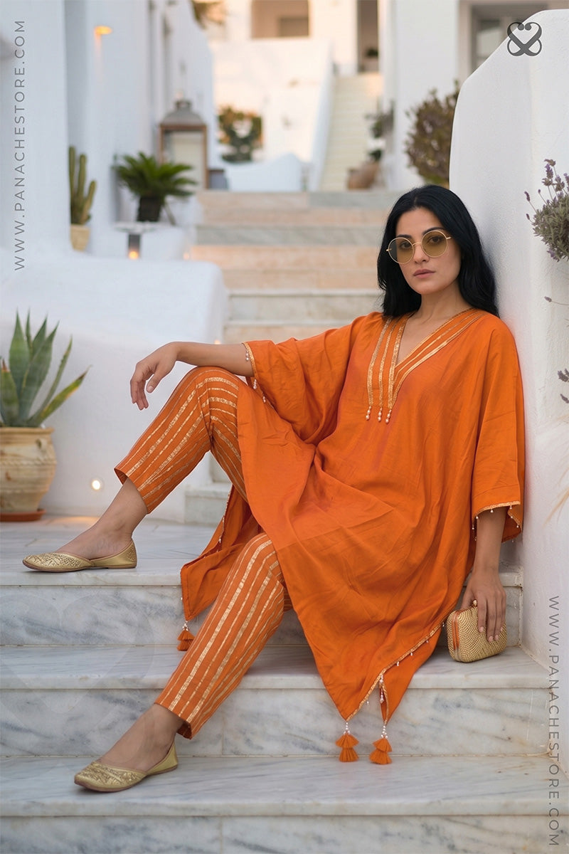 Woman in an orange Kaftan and zari strip orange pant outfit sitting on steps