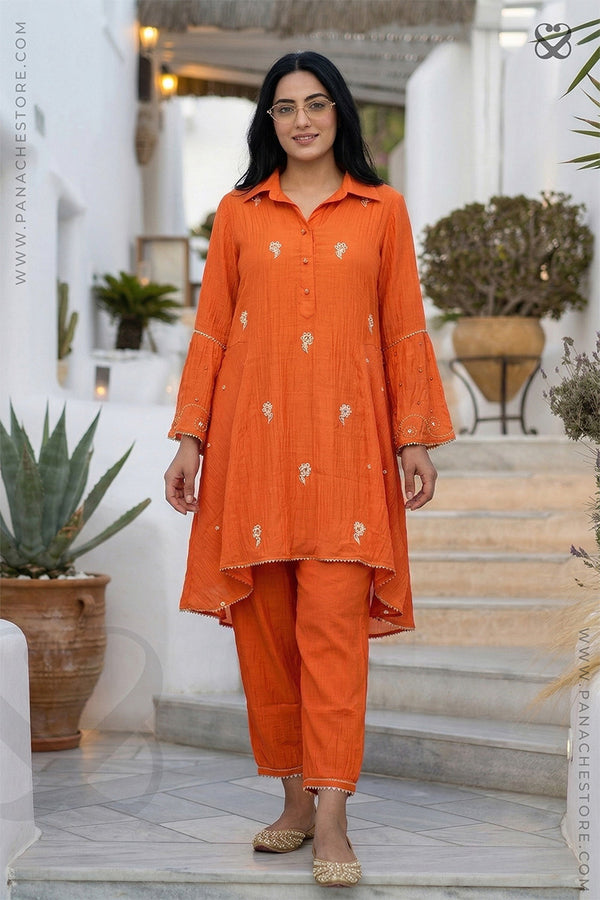 Woman in a orange kurti with zari embroidred motifs and matching pants standing on steps