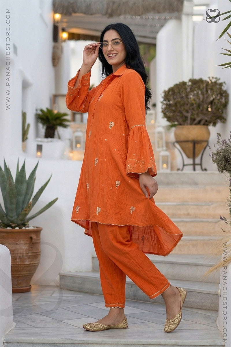 Woman in a orange kurti with zari embroidred motifs and matching pants standing on steps