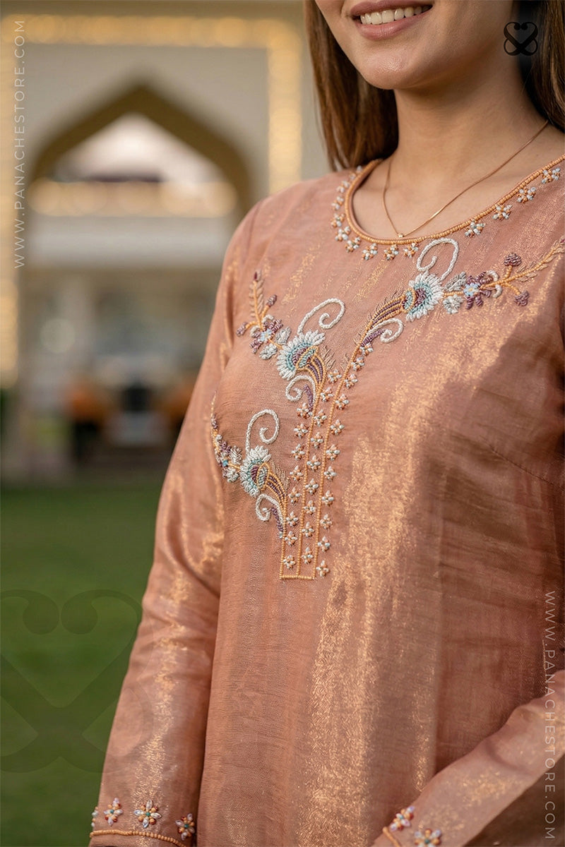 Close-up of a woman wearing a shiny peach floral embroidered kurti suit outfit with a blurred background.