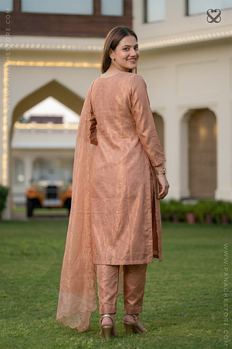 Woman in a peach traditional outfit standing on grass with a building in the background