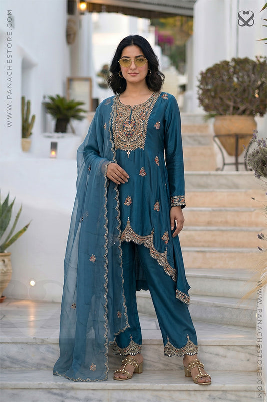 Woman in a teal blue designer salwar suit set outfit with gold embroidery standing on steps.