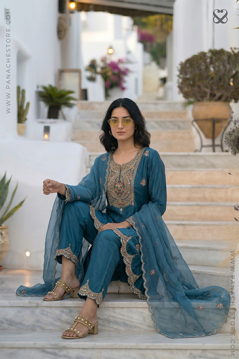 Woman in a teal blue designer salwar suit set outfit sitting on steps outdoors.