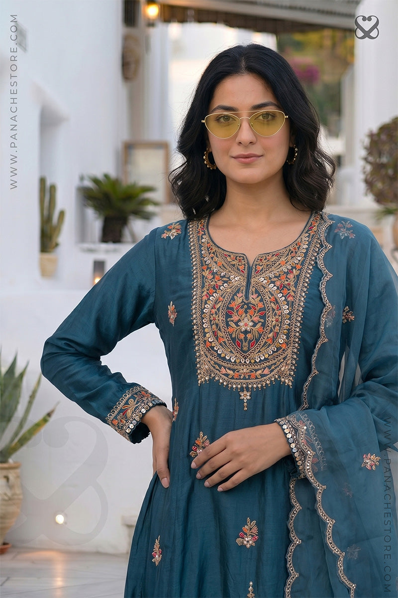 Woman wearing a teal embroidered designer salwar suit with a blurred indoor background
