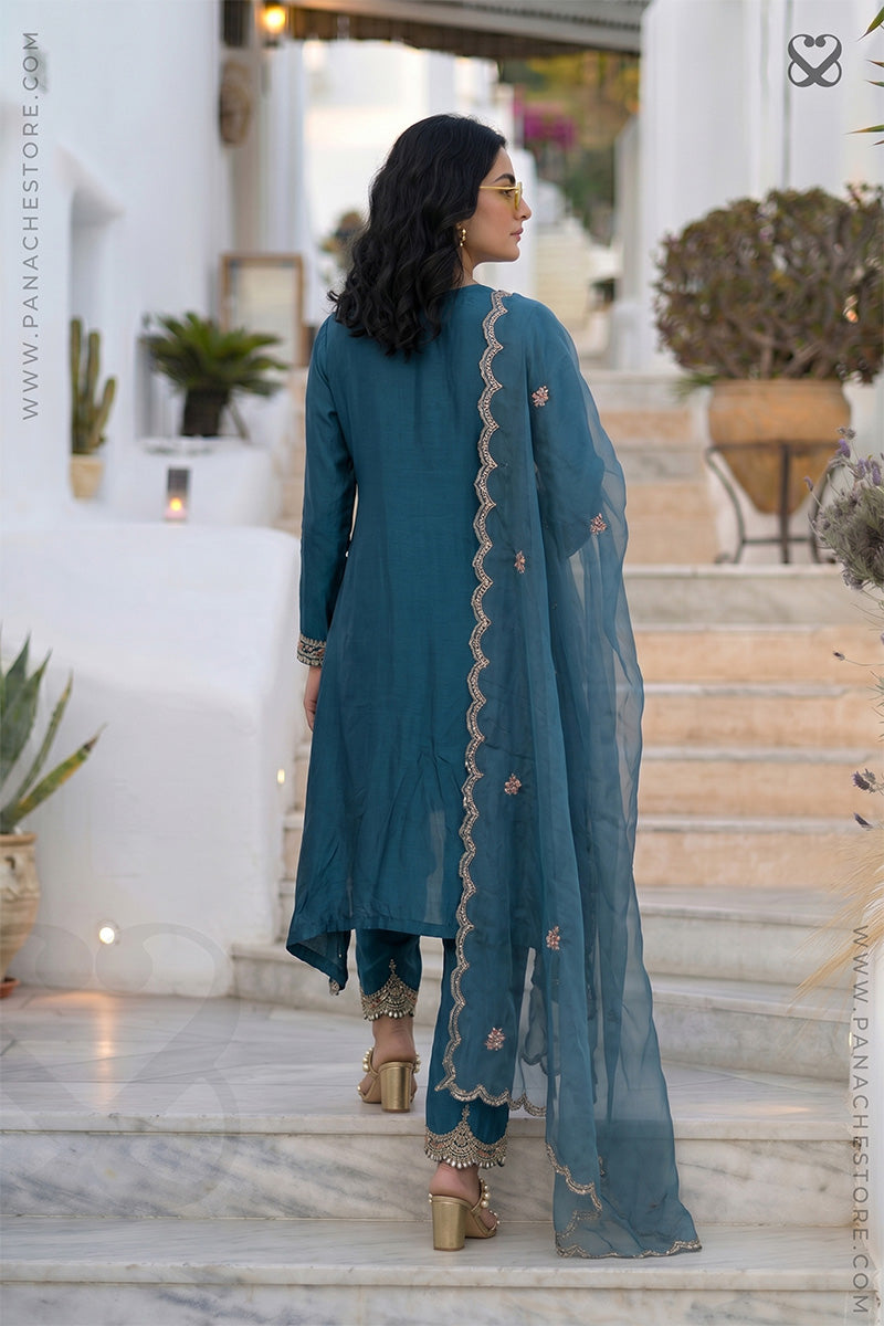 Woman in a teal outfit with floral patterns standing on steps outdoors.