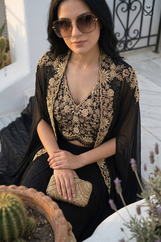 Woman wearing a black and gold embroidered designer shrug, crop top and black skirt sitting outdoors.