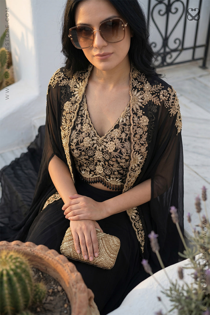 Woman wearing a black and gold embroidered designer shrug, crop top and black skirt sitting outdoors.