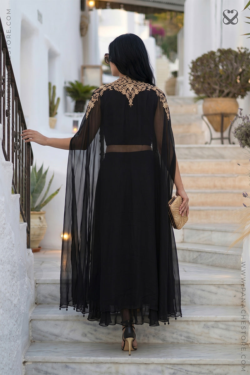 back pose of a woman in a designer capeclimbing on steps with plants in the background