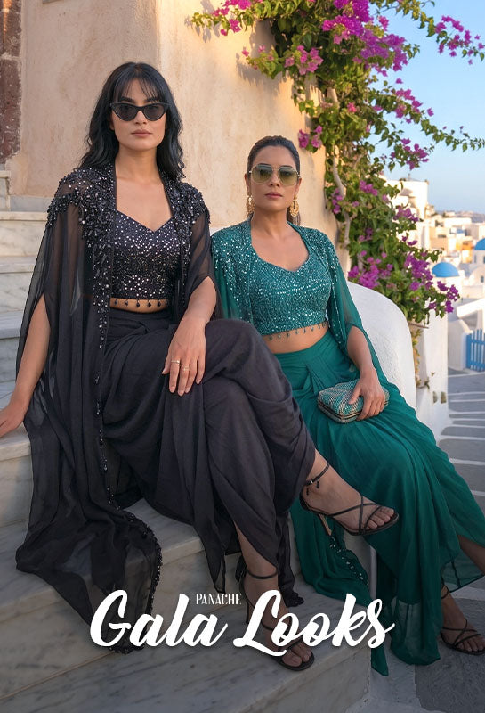 Two women in designer Cap outfit set attire sitting on a steps with a scenic ocean view and 'Gala Looks' branding.