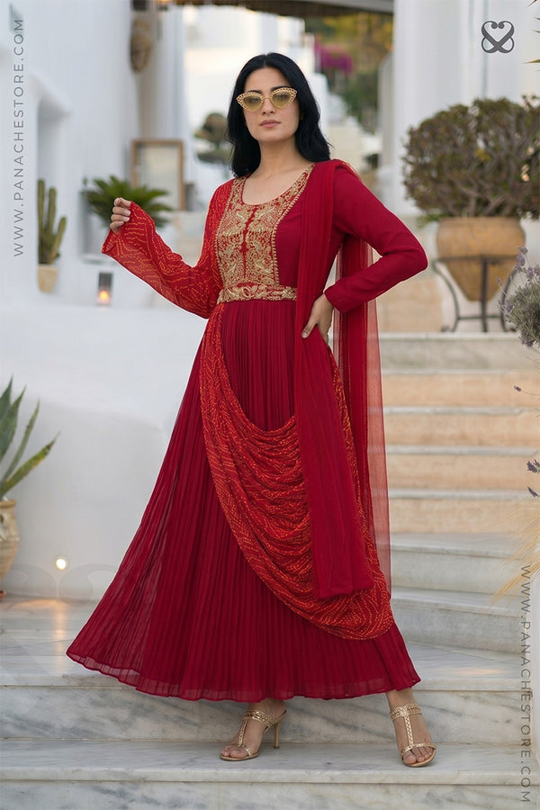 Woman in a red modern traditional dress with gold embroidery and bandhani print standing on steps