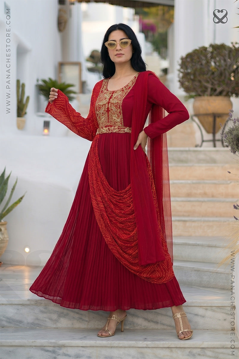 Woman in a red modern traditional dress with gold embroidery and bandhani print standing on steps