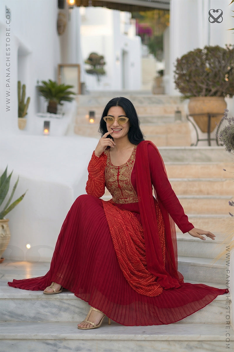 Woman in a red modern traditional dress with gold embroidery and bandhani print sitting on steps
