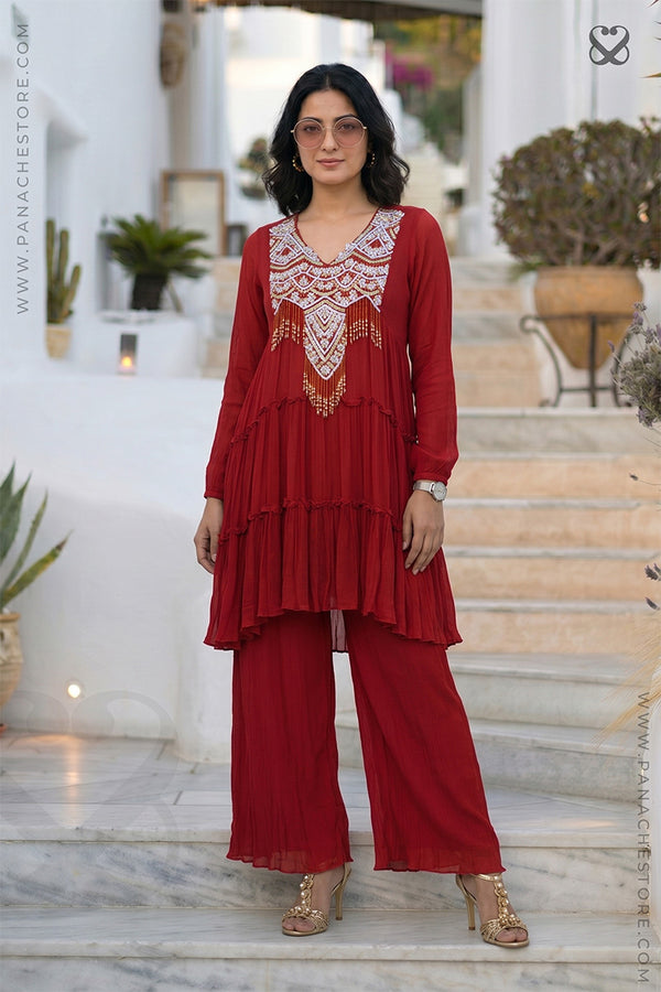 Woman in a red modern yet traditional outfit with intricate neckline patterns standing on steps outdoors.