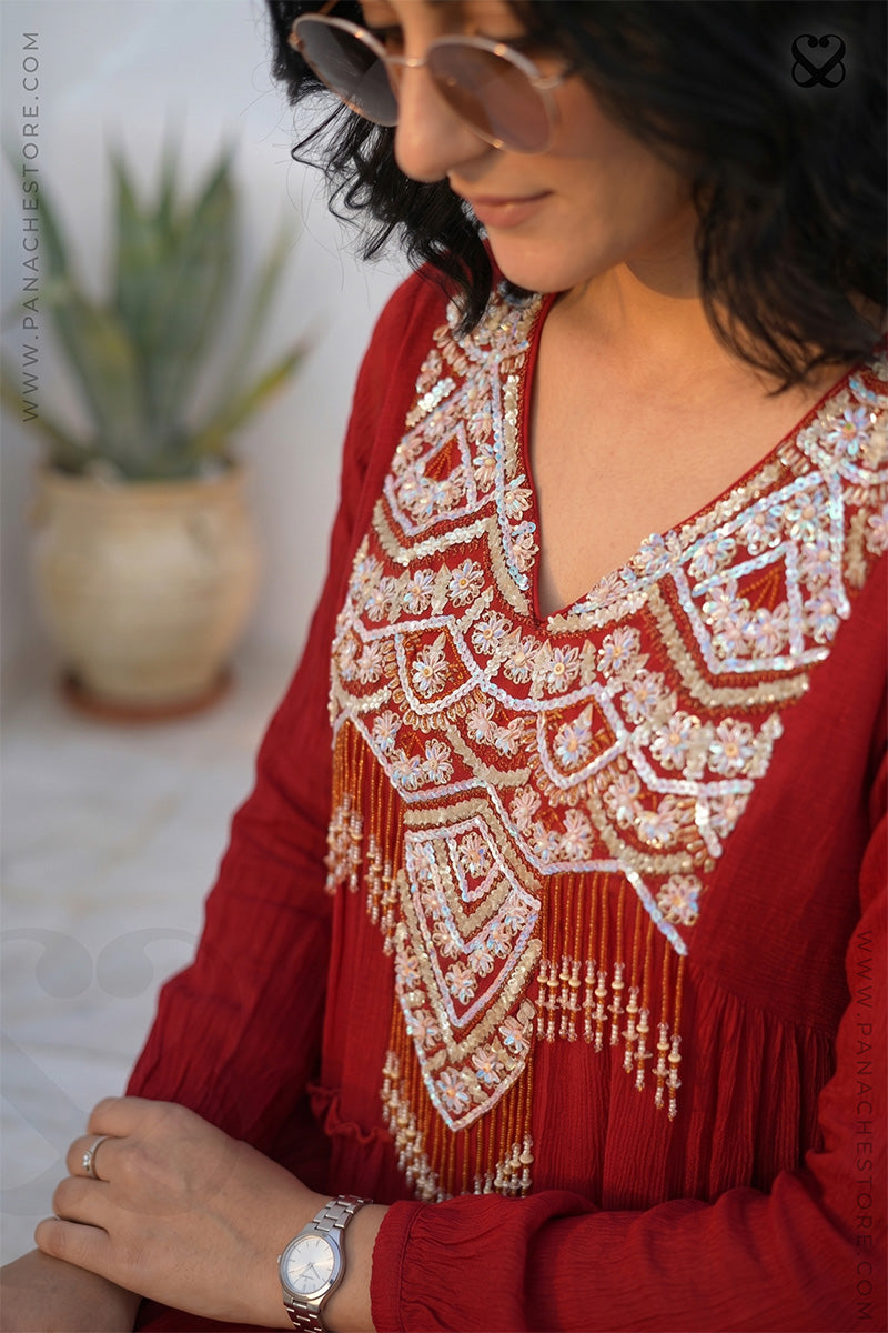 Woman wearing a red embroidered top with a plant in the background