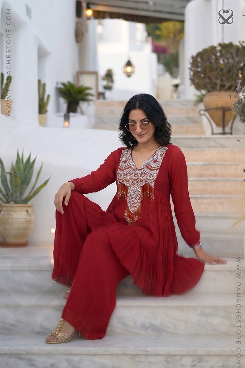 Woman in a red modern yet traditional outfit with intricate neckline patterns sitting on steps outdoors.