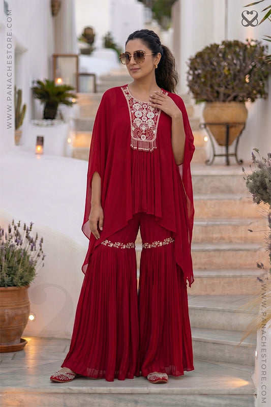 Woman in a red outfit with white floral embroidery standing on steps in an outdoor setting.
