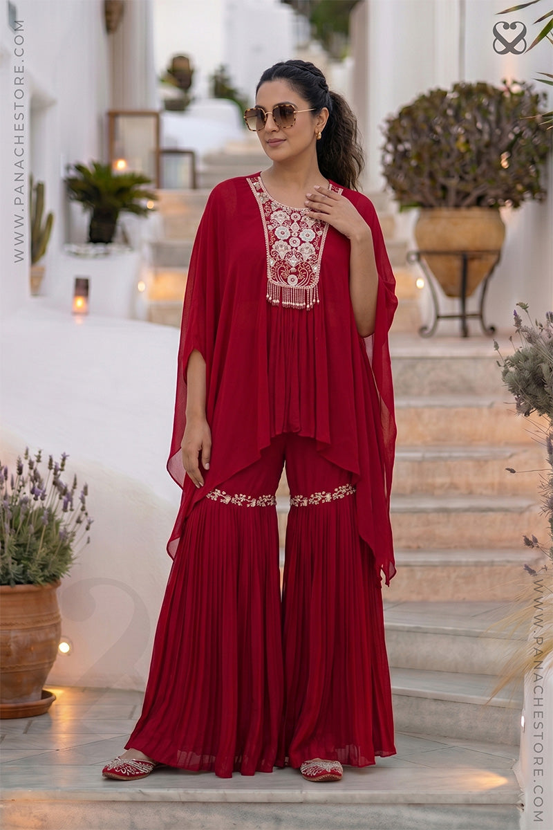 Woman in a red outfit with white floral embroidery standing on steps in an outdoor setting.