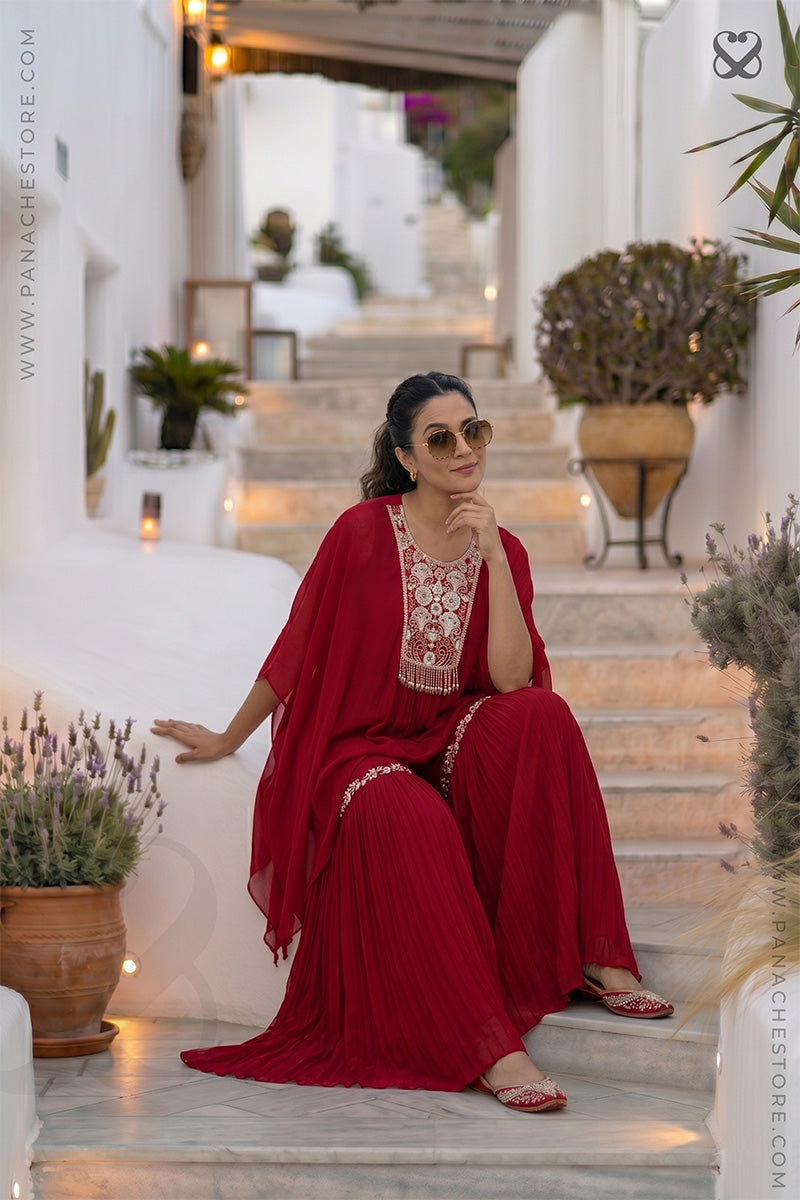 Woman in a red outfit with white floral embroidery sitting on steps in an outdoor setting.