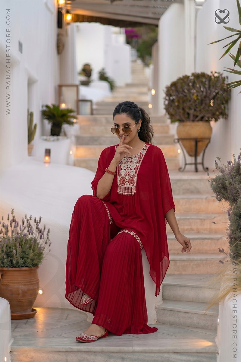 Woman in a red outfit with white floral embroidery sitting on steps in an outdoor setting.