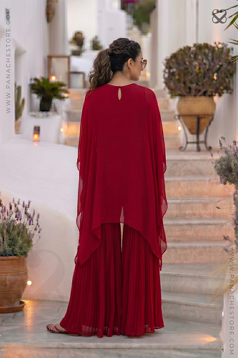 Woman in a red outfit standing on a staircase with decorative plants and lights in the background.
