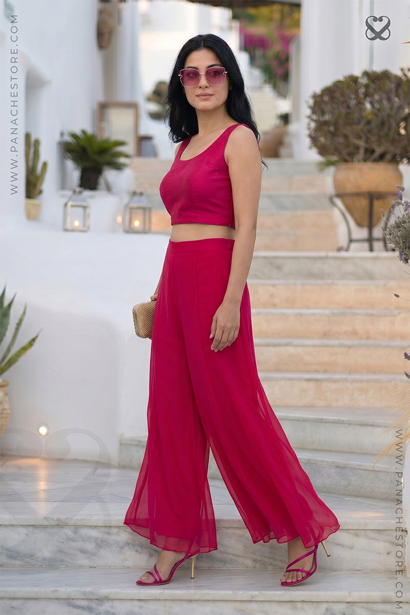 Woman in a red-pink bustier blouse and plazo plant outfit set standing on steps with a blurred background