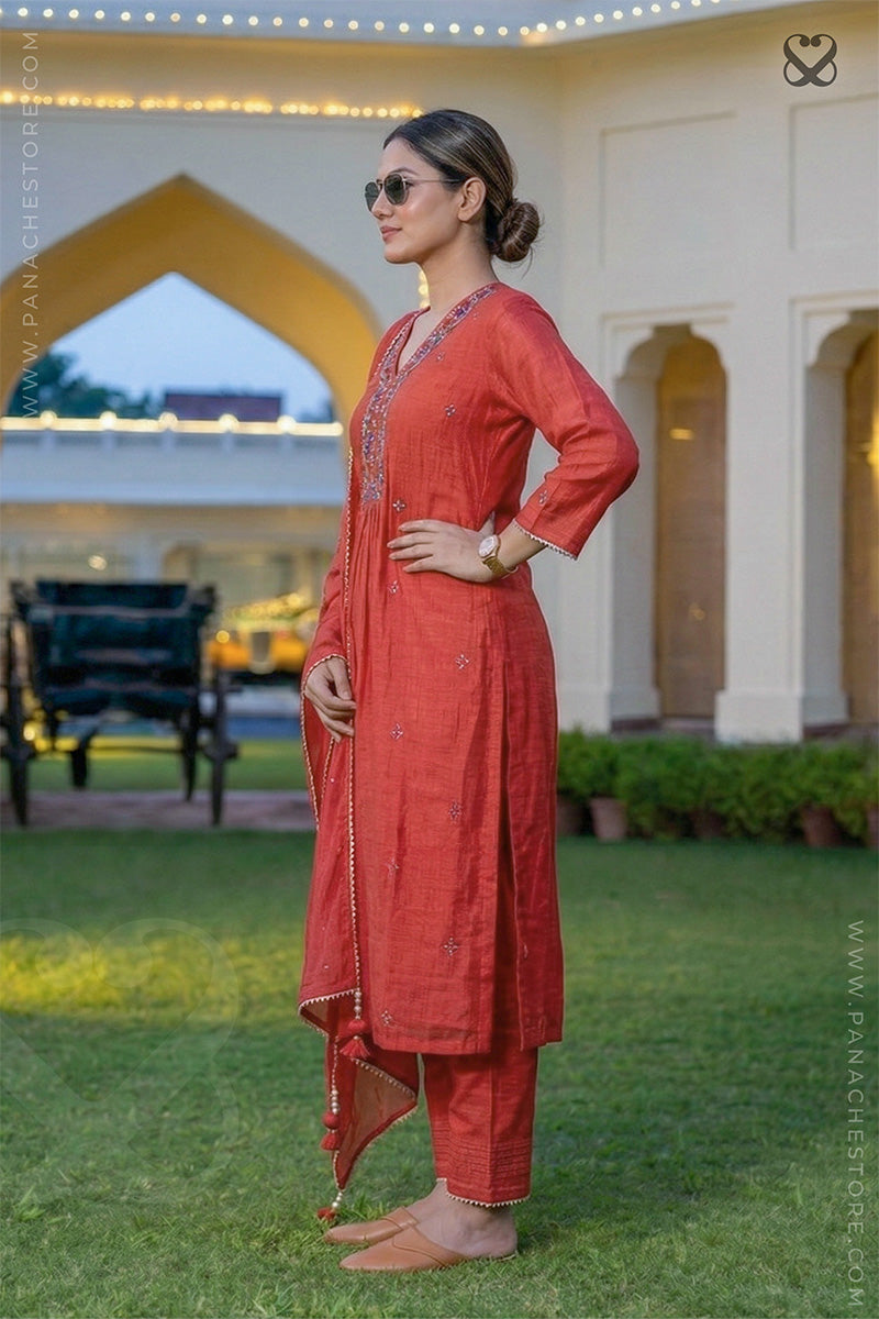 Woman in a red salwar suit set with dupatta standing side pose in garden
