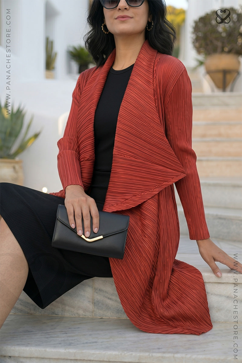 Woman wearing a red textured outfit with a black clutch, sitting outdoors.