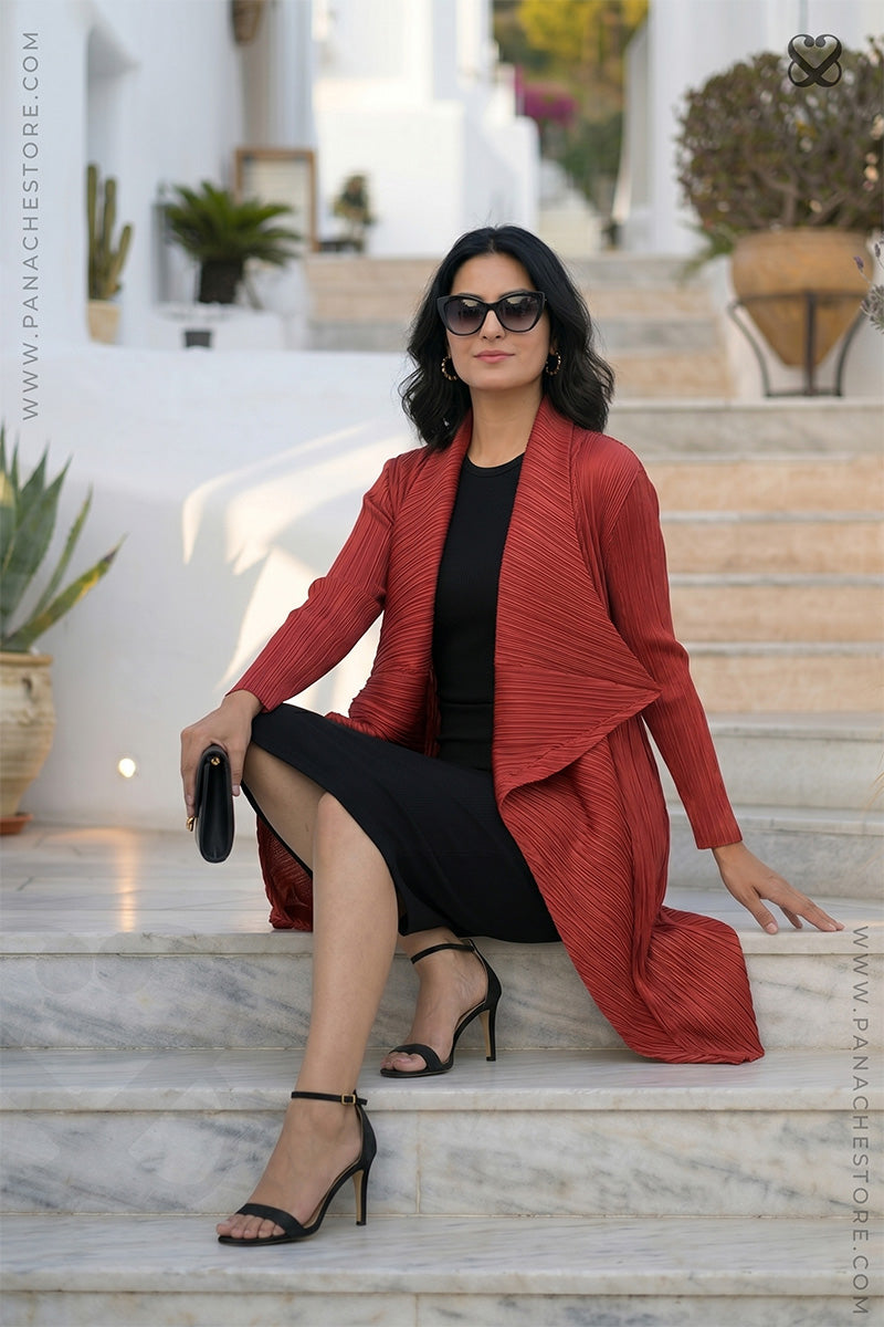 Woman in a red shrug jacket and black dress sitting on marble steps with a blurred background
