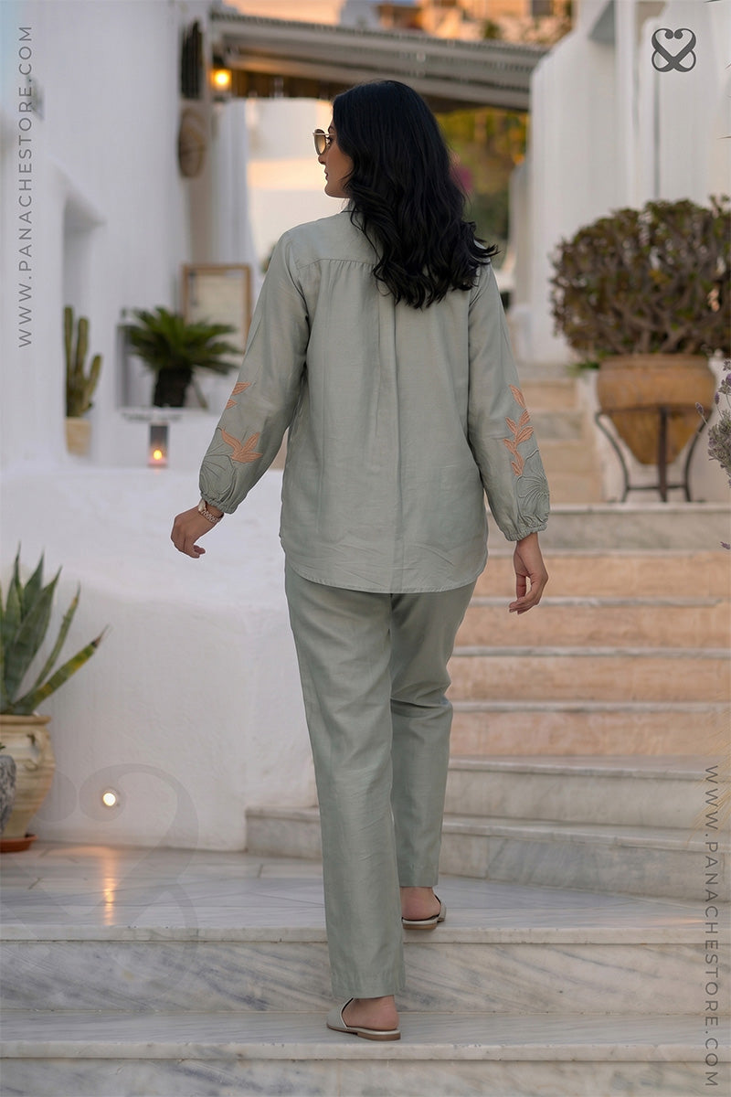Woman in a light green co ord outfit set with floral embroidery & aplique work standing on steps