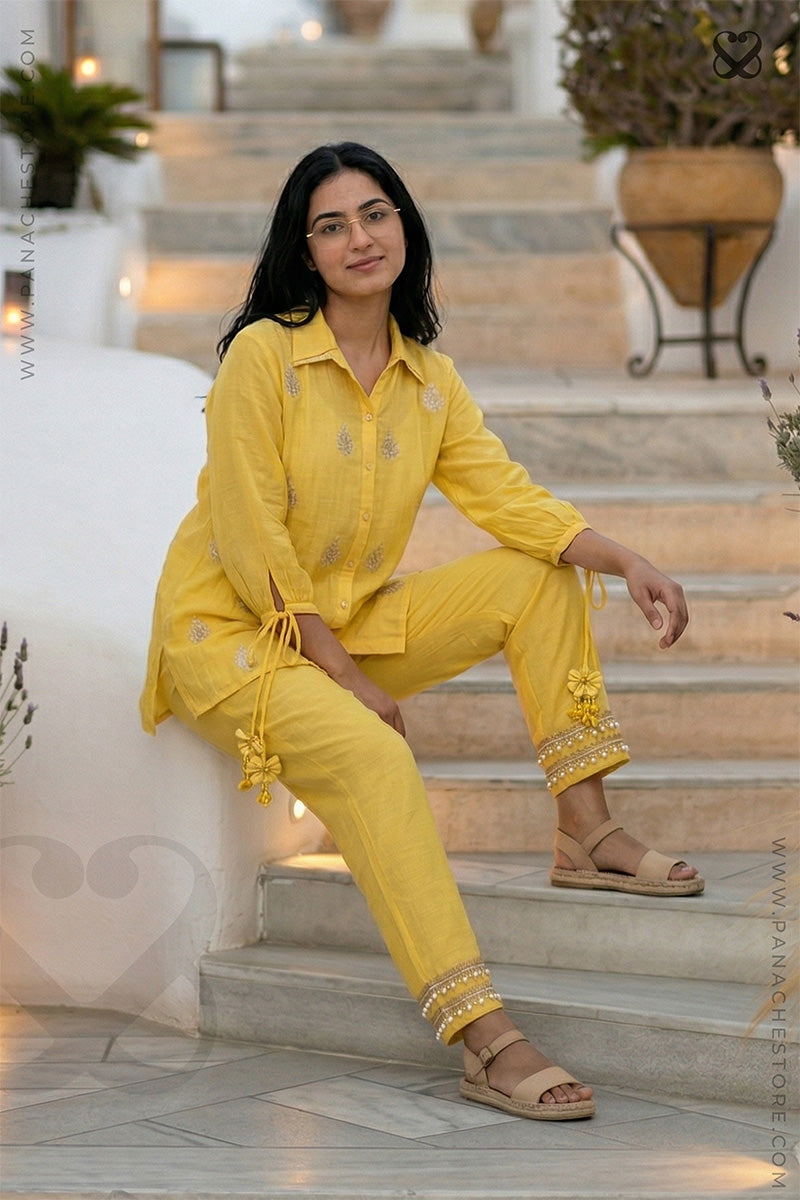 Woman in a yellow shirt with zari motifs with unique hand cuf sleeve design and matching pants sitting on steps