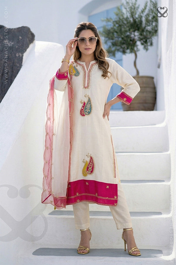 Woman in cream white slawar suit set with pink embellishments and pink dupatta standing on step
