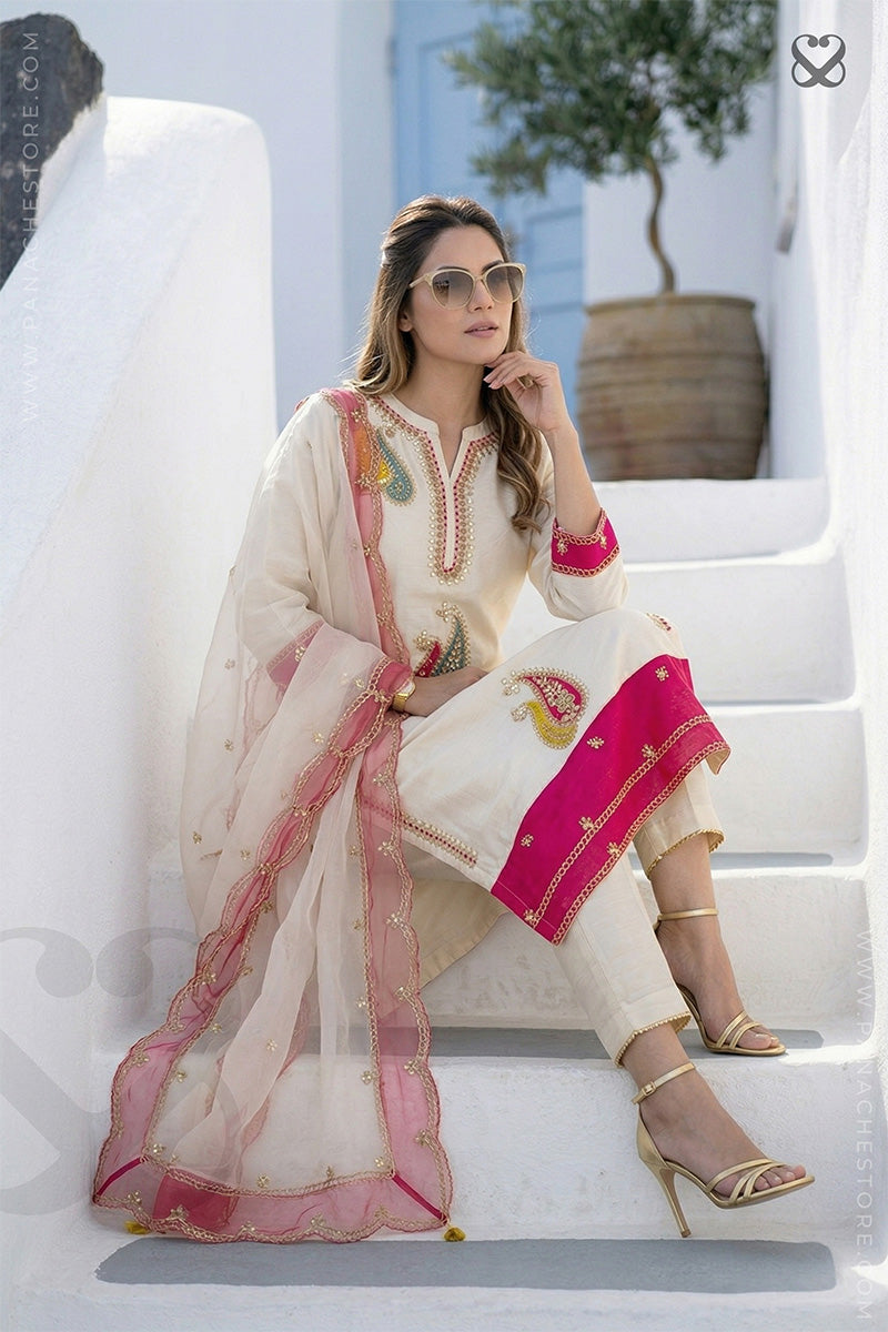 Woman in cream white slawar suit set with pink embellishments and pink dupatta sitting on steps