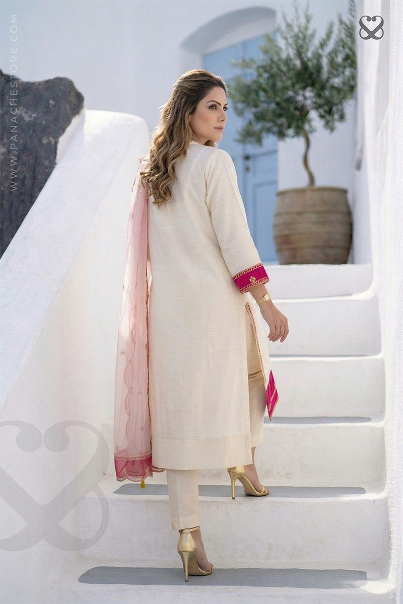 Woman in cream white slawar suit set with pink accents and pink dupatta standing on grass