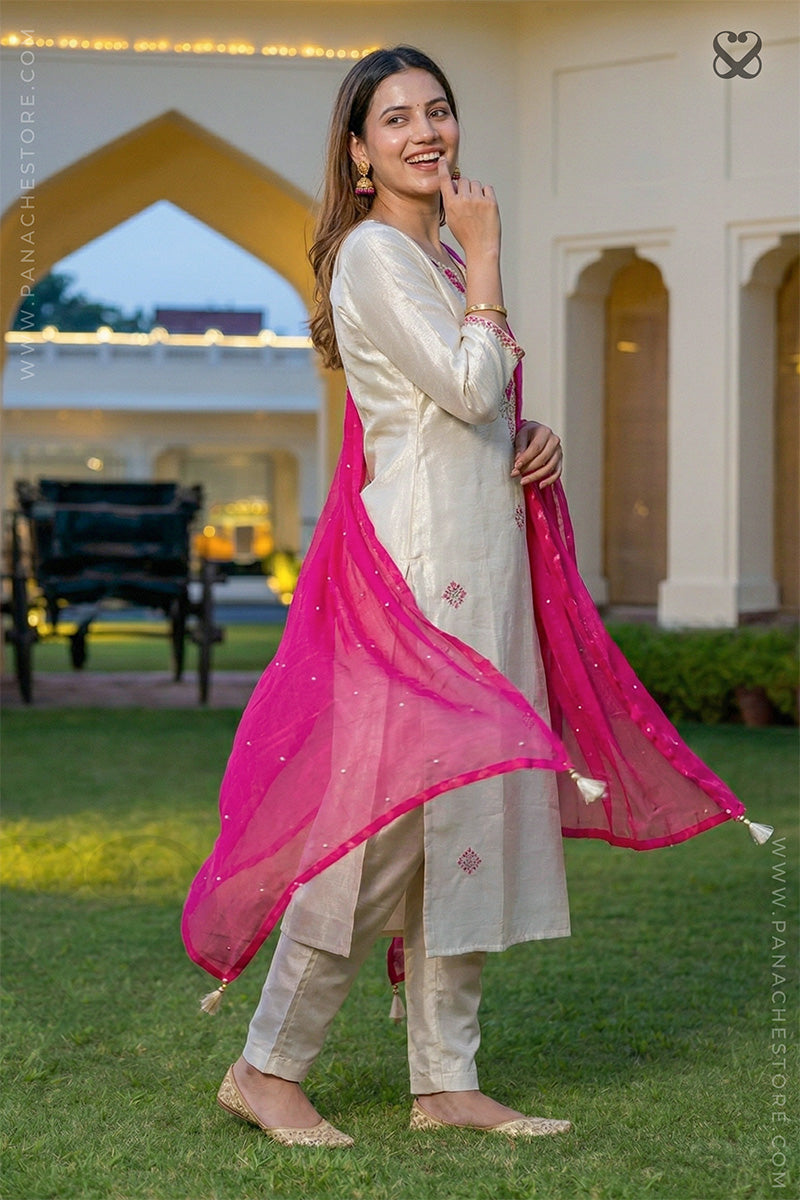 Woman in a cream salwar suit set with pink dupatta standing in garden