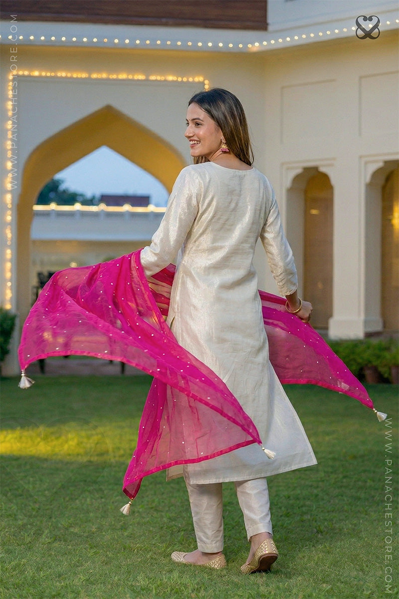 Woman in a cream salwar suit set with pink dupatta dancing in garden