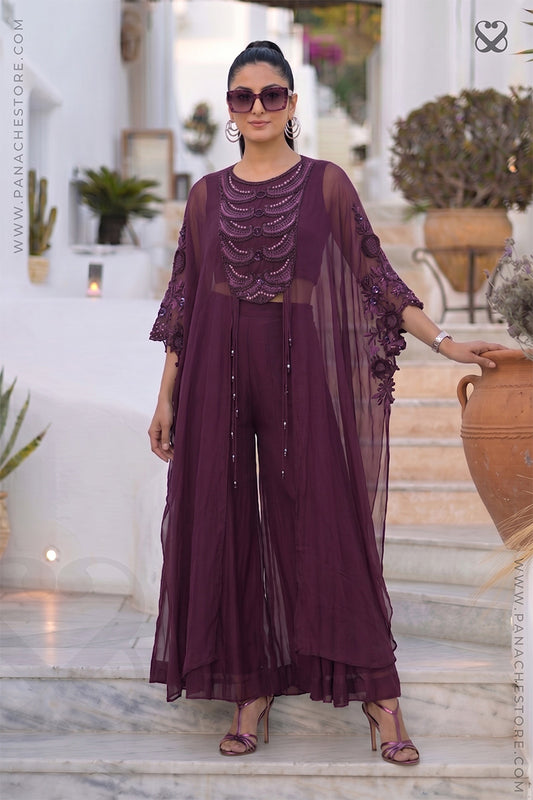 Woman in a purple-wine designer Kaftan outfit standing outdoors with decorative elements.