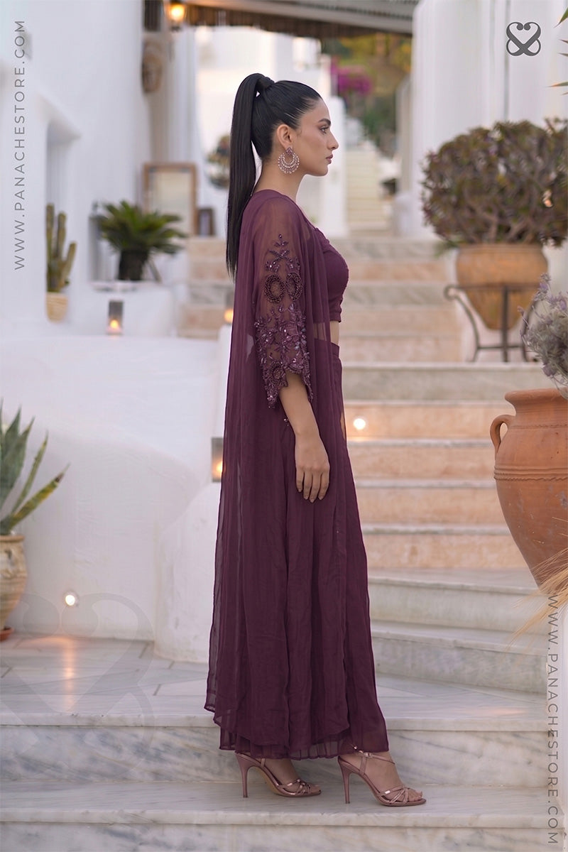 Woman in a long, dark wine kaftan dress standing on a marble staircase with decorative plants and a building in the background.