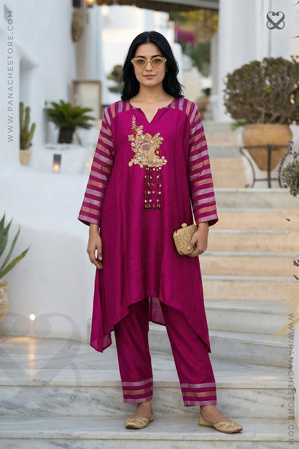 Woman wearing a magenta pink traditional kurti pant set with gold embroidery on a marble staircase.