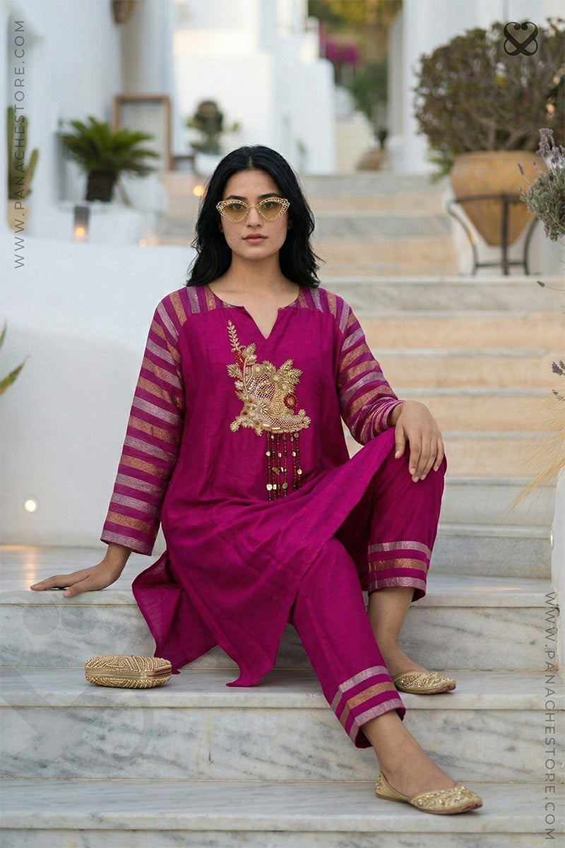 Woman wearing a magenta pink traditional kurti pant set with gold embroidery sitting on a marble staircase.
