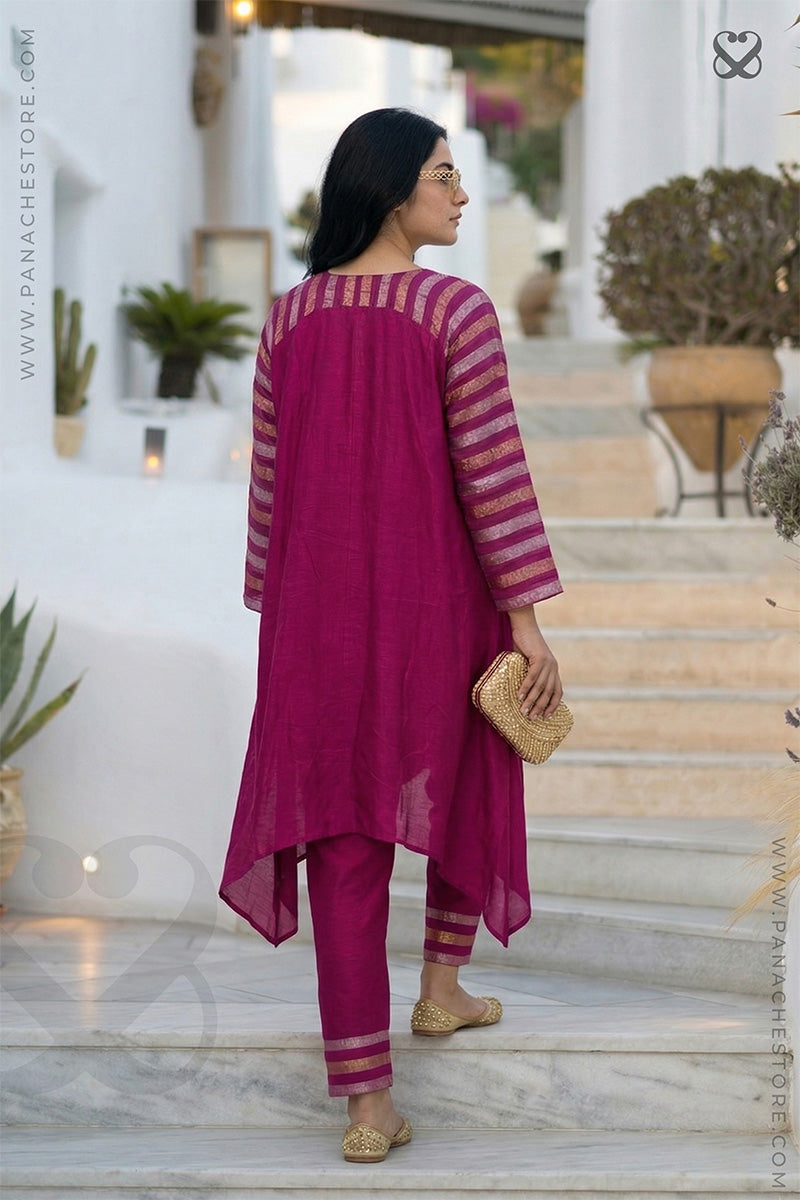 Woman wearing a magenta pink traditional kurti pant set with gold embroidery climbing on a marble staircase.