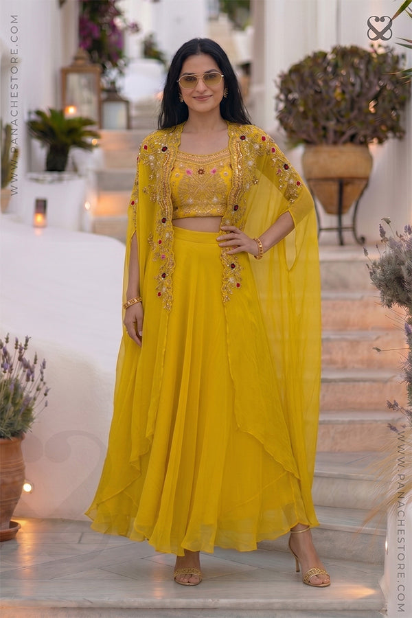Woman wearing a designer yellow embroidered shrug & blouse outfit with zardozi and meenakari work and yellow skirt standing on steps
