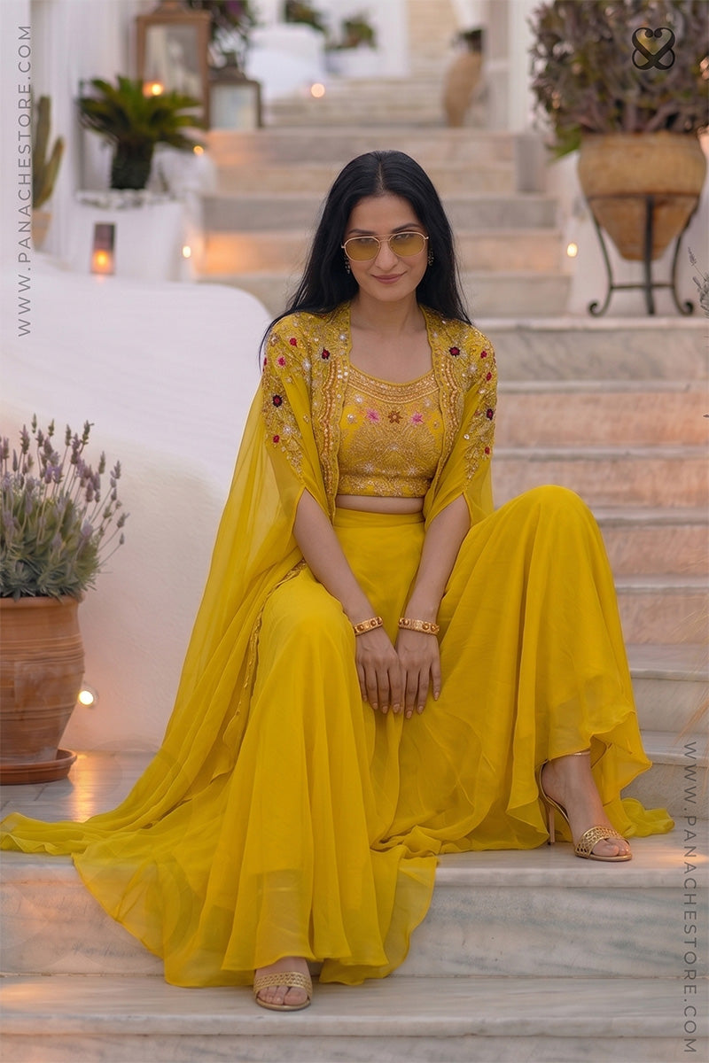 Woman wearing a designer yellow embroidered shrug & blouse outfit with zardozi and meenakari work and yellow skirt sitting in steps
