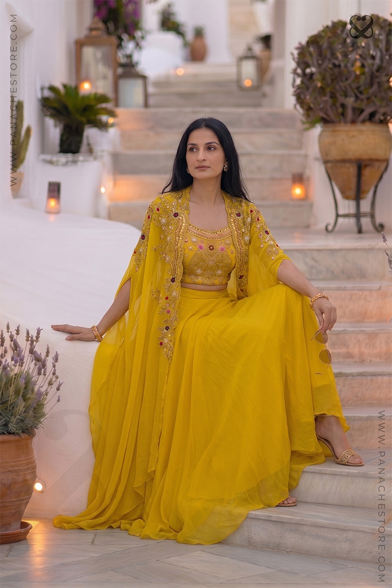 Woman wearing a designer yellow embroidered shrug & blouse outfit with zardozi and meenakari work and yellow skirt sitting in steps