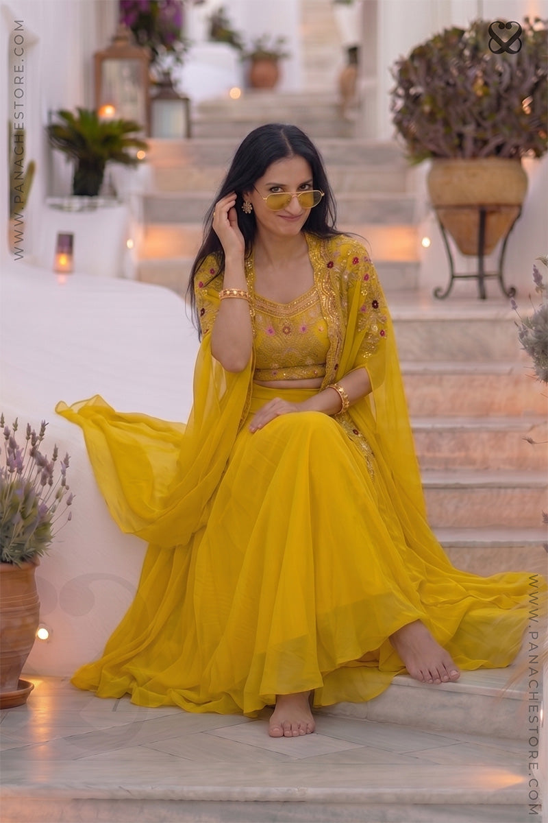 Woman wearing a designer yellow embroidered shrug & blouse outfit with zardozi and meenakari work and yellow skirt in an outdoor setting