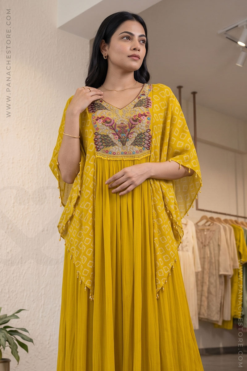 A woman models a vibrant yellow traditional Indian dress with a heavily embroidered floral bodice and a matching sheer printed dupatta, set against a softly blurred boutique background.