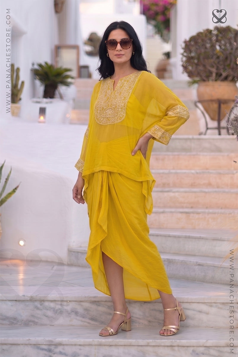 Woman wearing a yellow kaftan outfit with white embroidery standing on step