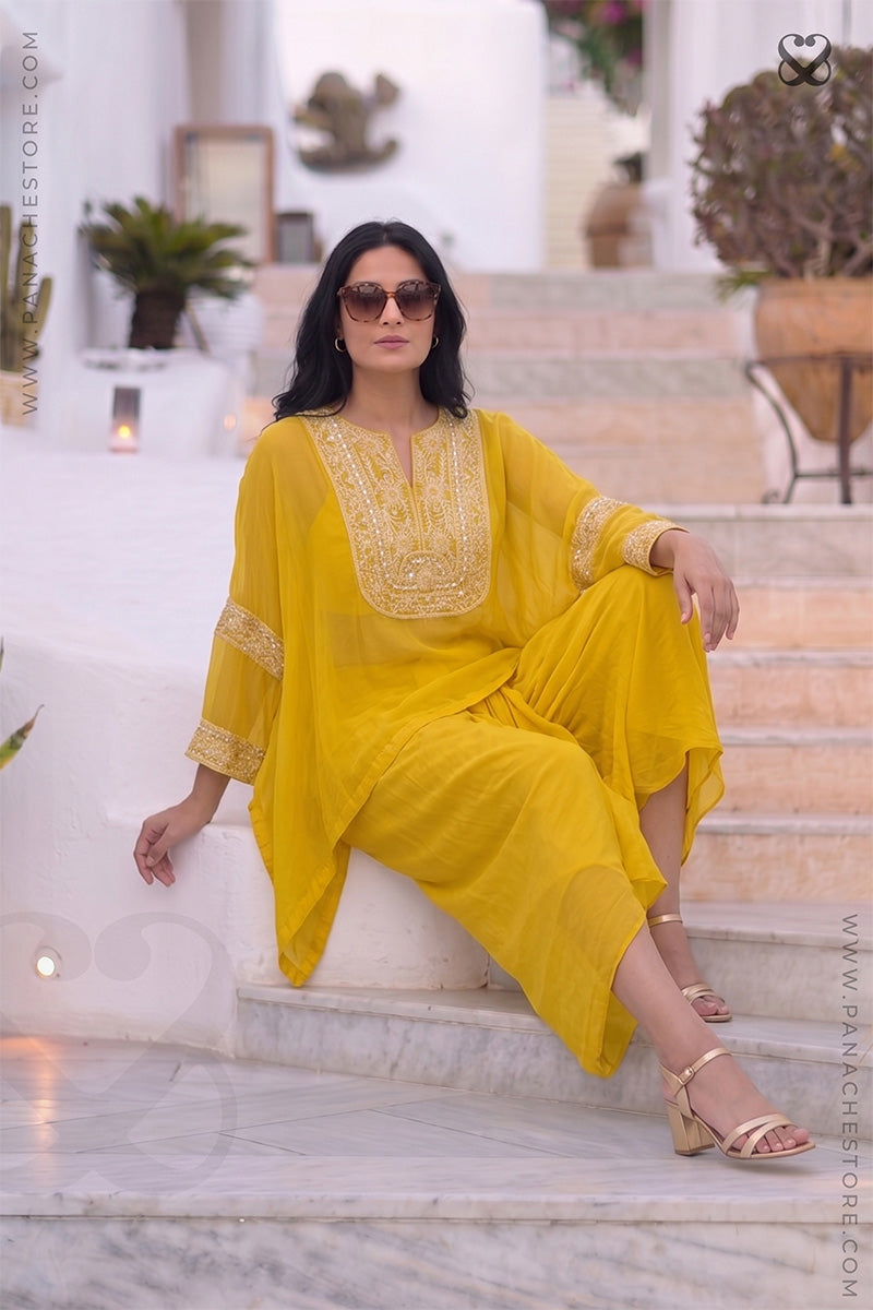 Woman wearing a yellow kaftan outfit with white embroidery sitting  on step